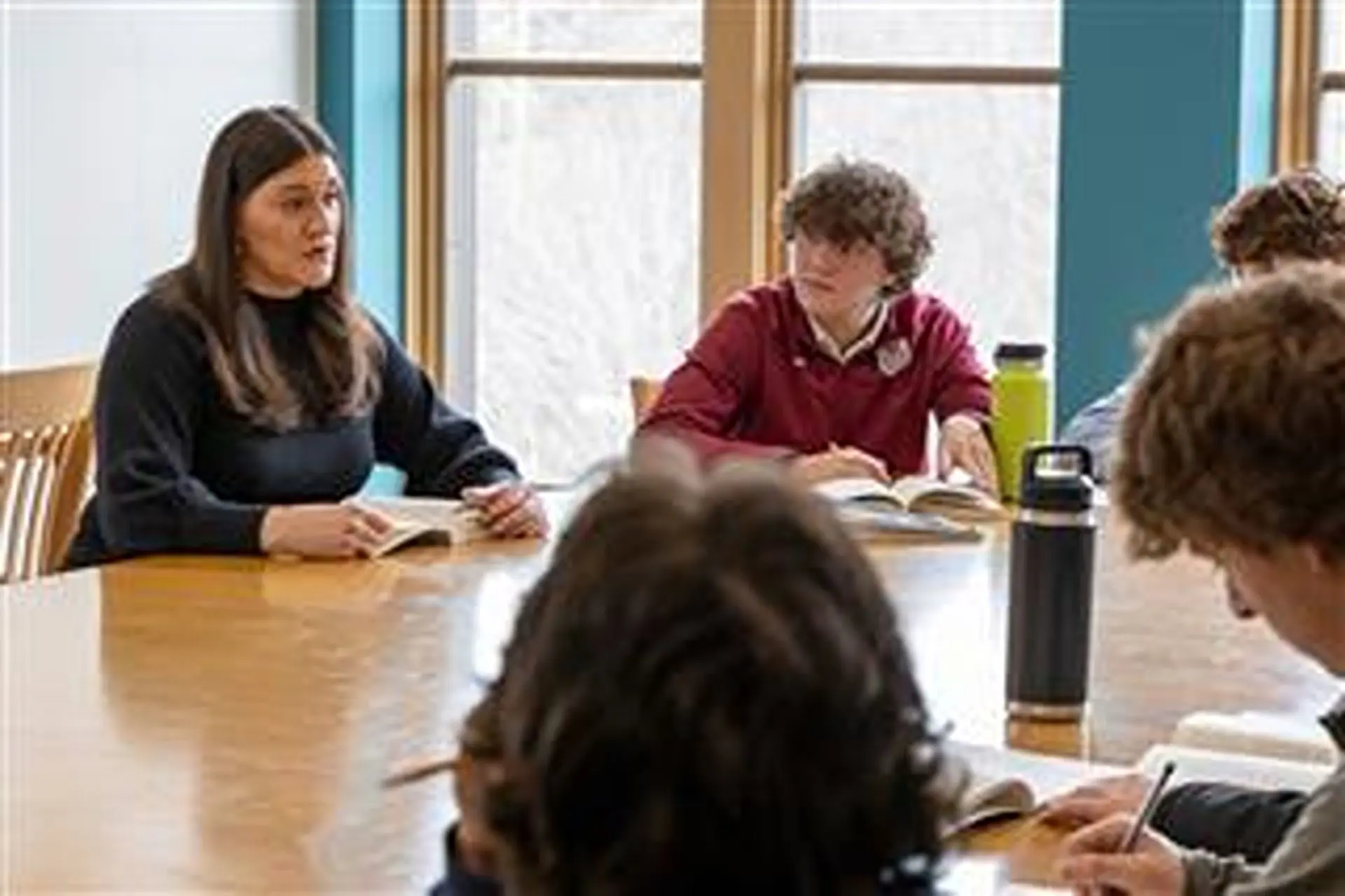 Ashley Worthington leading students in a discussion in an English lesson, seated at a wooden table with open books.