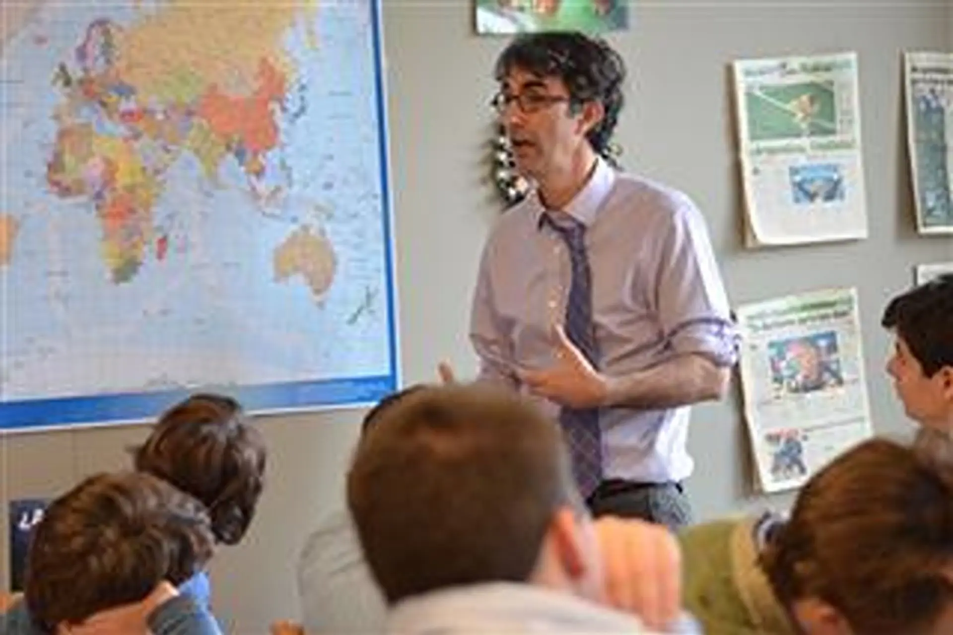 Peter Millett speaking to a class during a language lesson in a classroom with a world map on the wall.