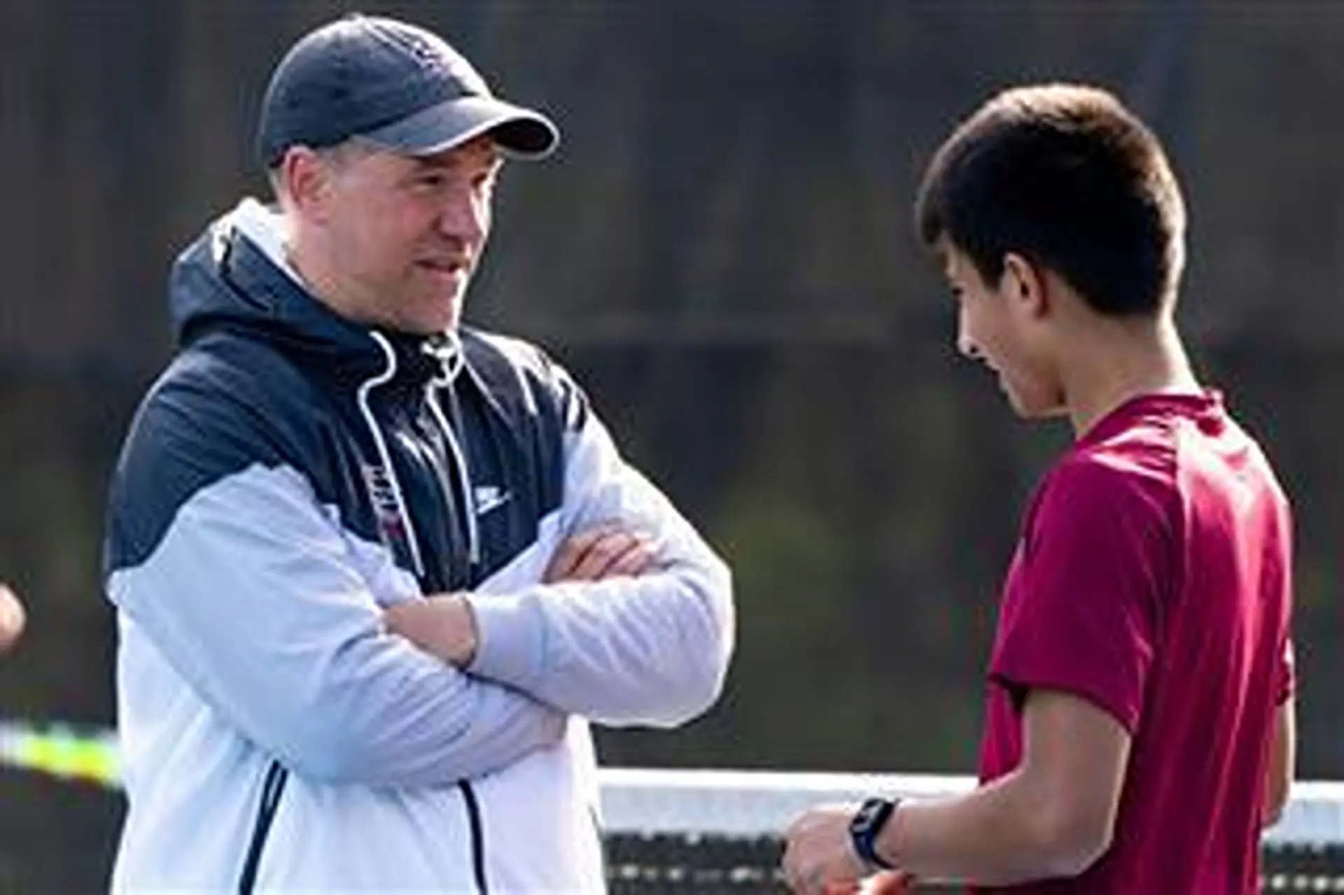 Adam Atwell talking to a student on a tennis court.