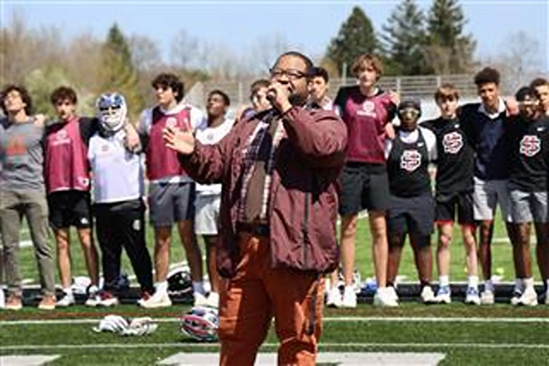 Devon Steve '13 speaking through a microphone on the sports pitch at a school event.