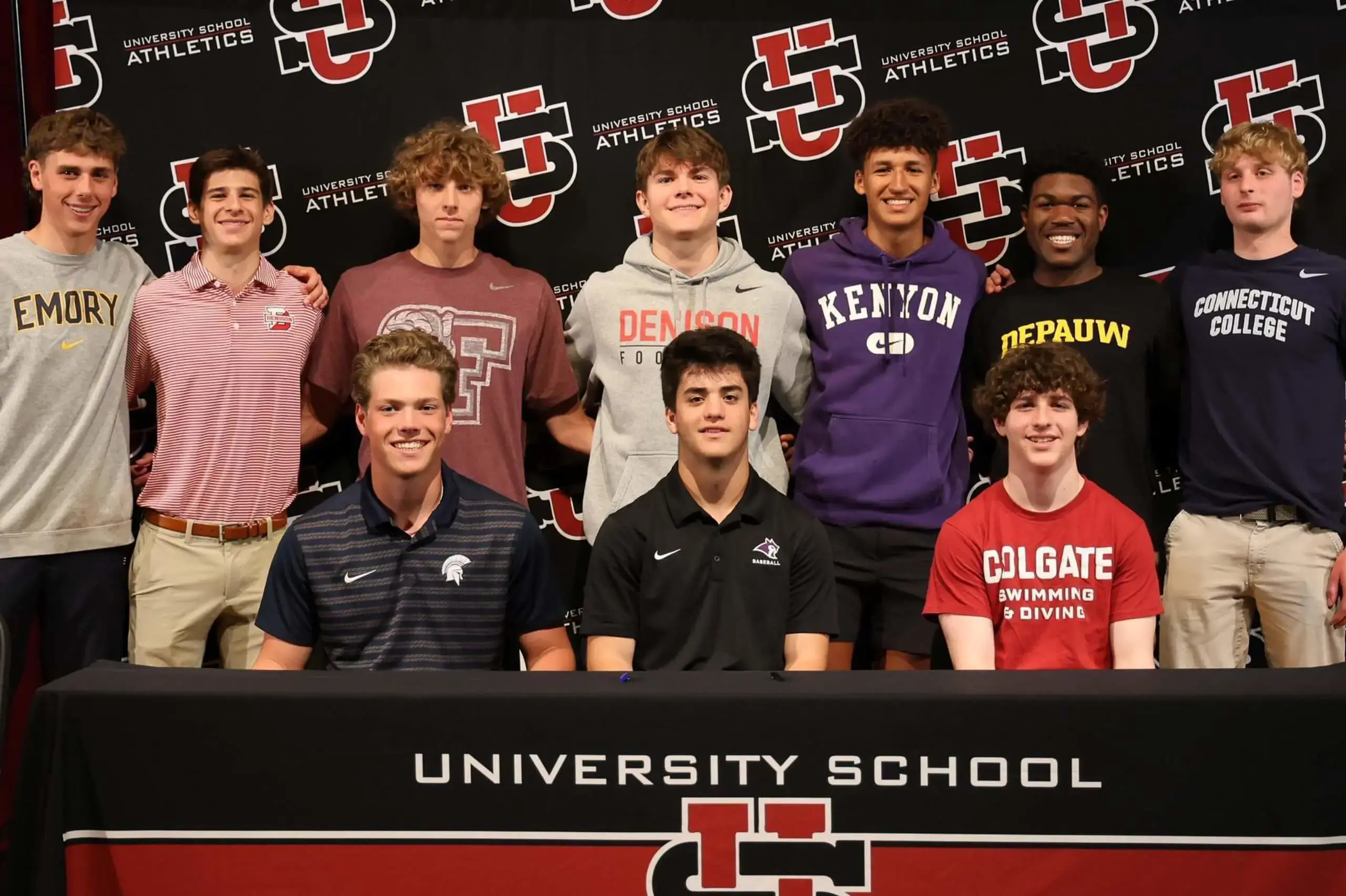 University School 2025 Collegiate Athletes wearing their college sweaters and posing for a photograph with a university school brand backdrop.