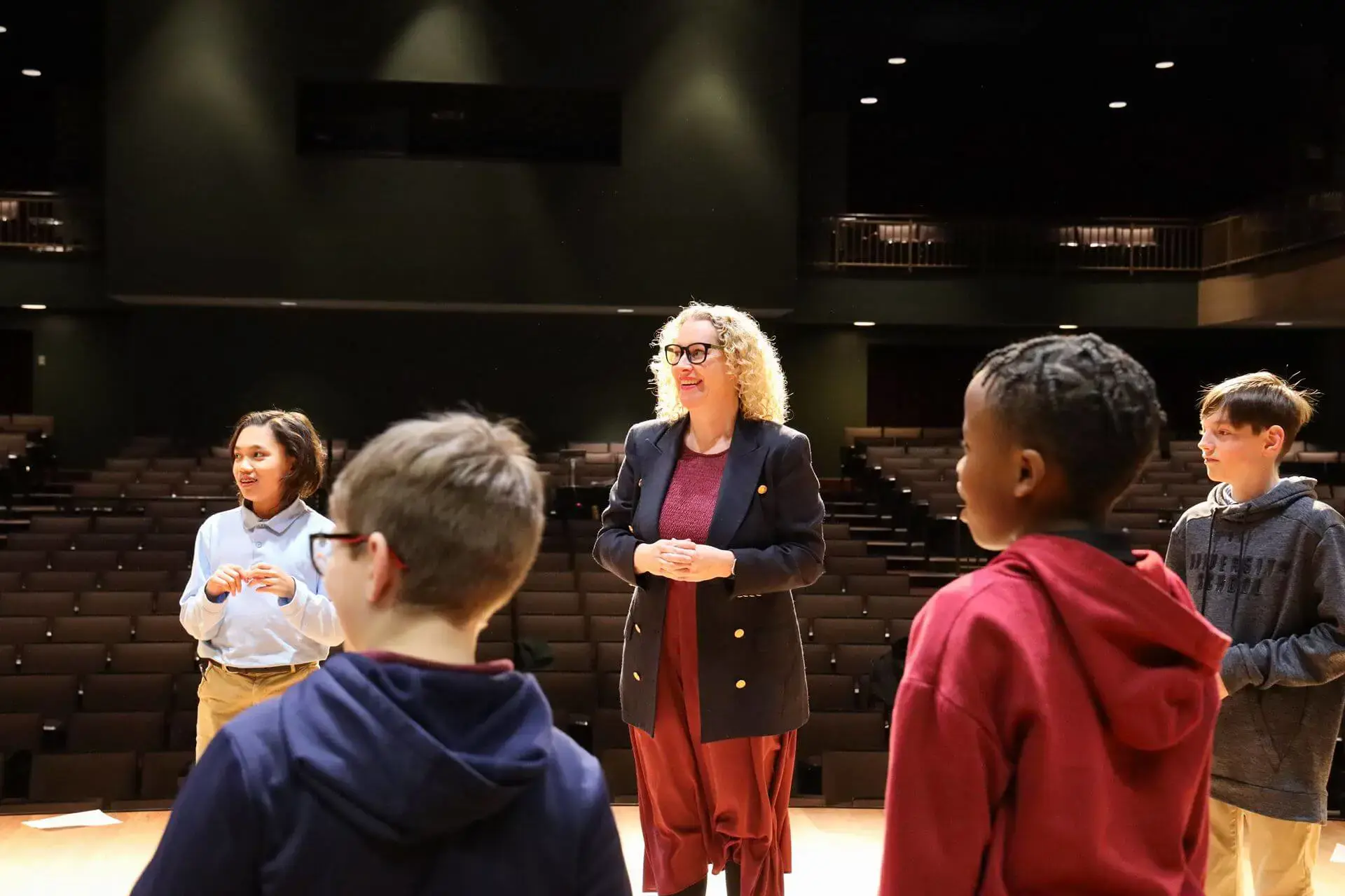Middle School Theatre teacher and students stand on stage together, smiling happily.
