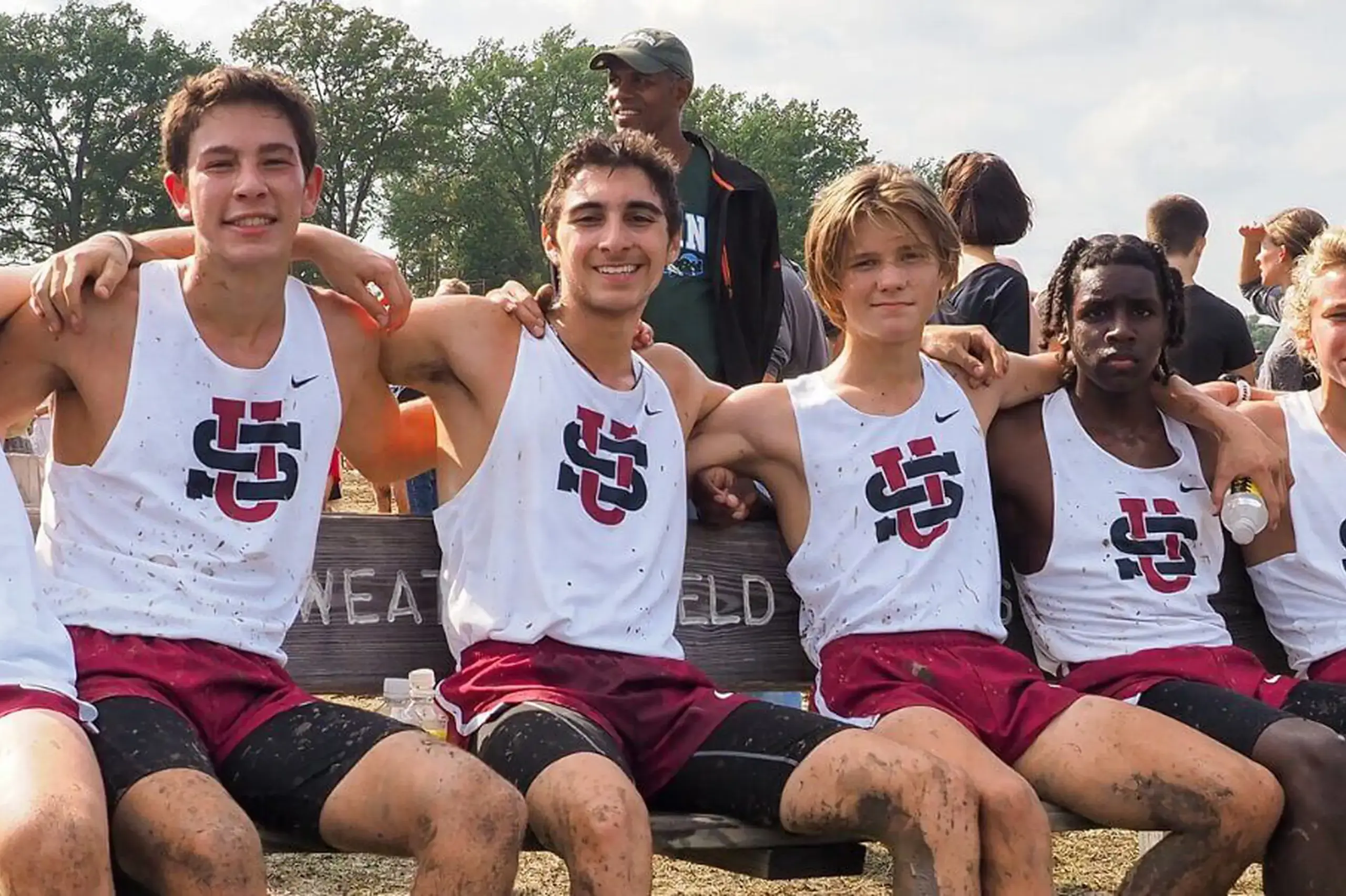 University School student Cross Country team pose for a photograph arm in arm and smiling happily after running a race.