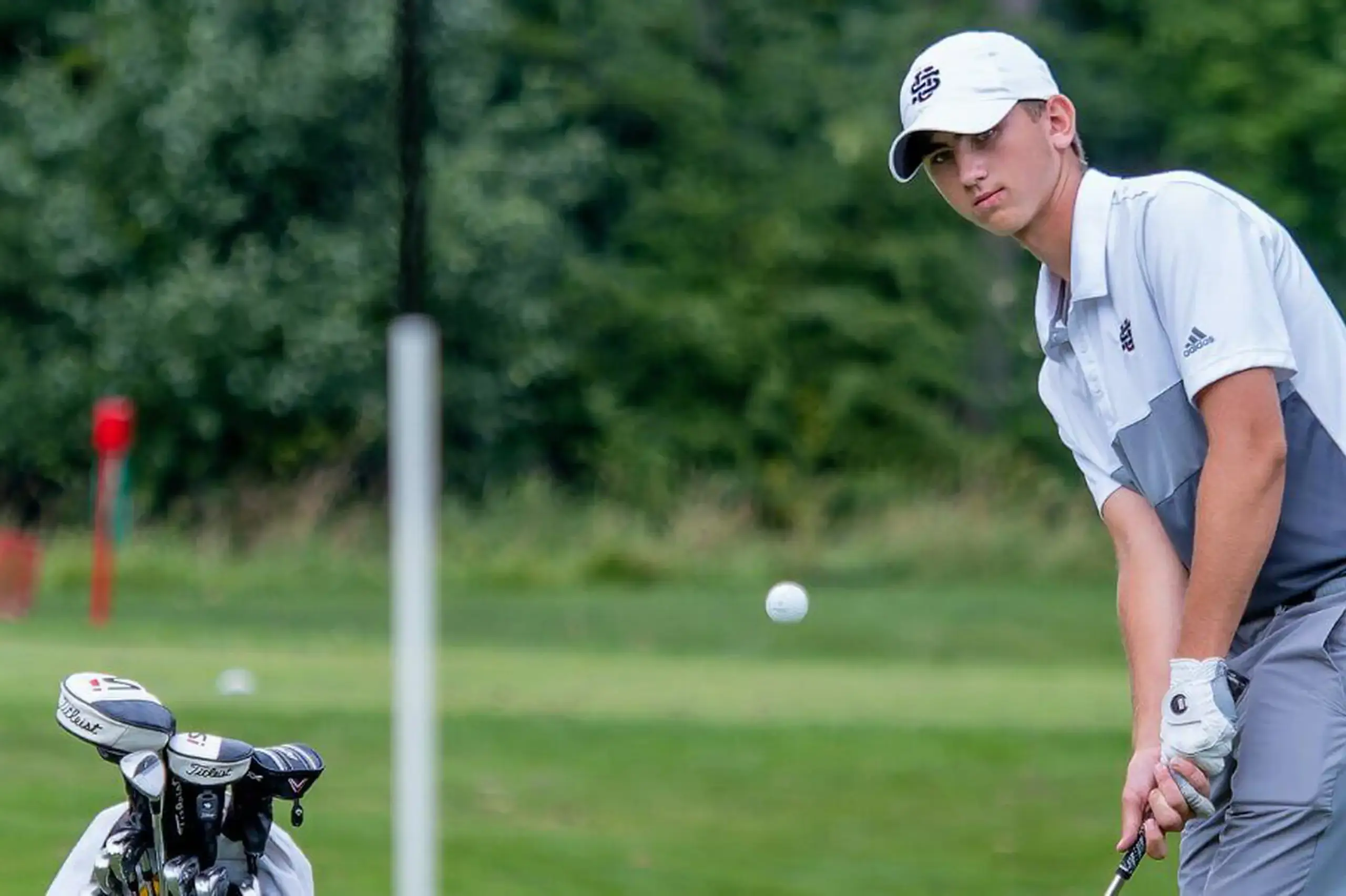 University School student wearing a baseball cap swings a golf club on a golfing green.
