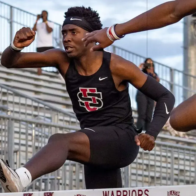 University School student leaping over hurdles during a track and field event, wearing a University School athletics uniform.