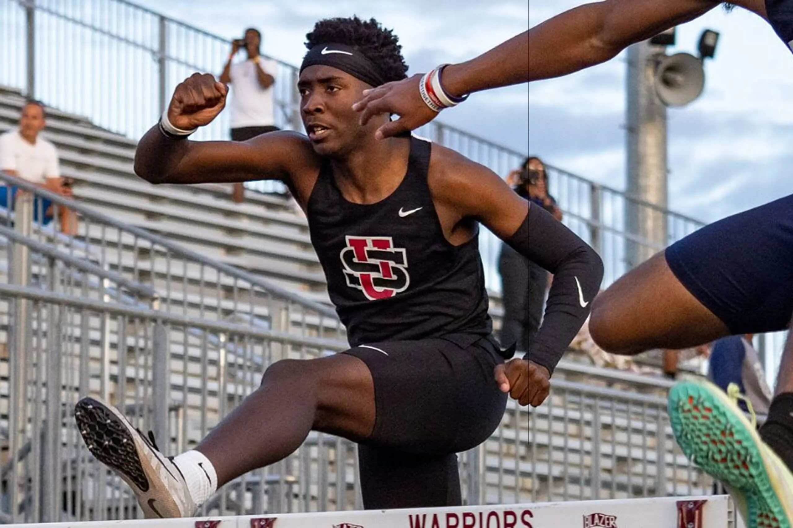 University School student leaping over hurdles during a track and field event, wearing a University School athletics uniform.
