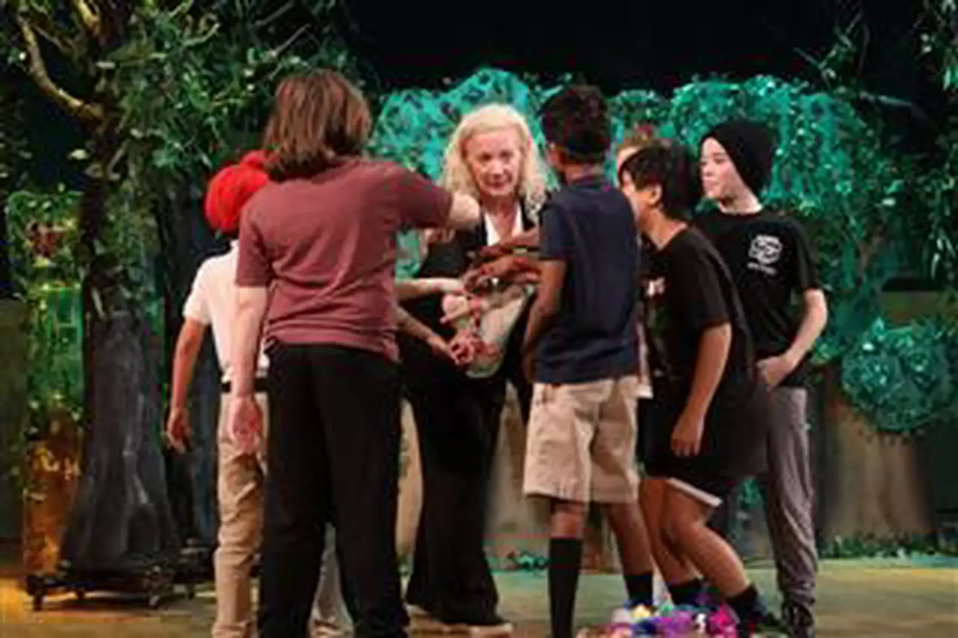 Shirley Veness in a hand stack huddle with students on a theatre set.