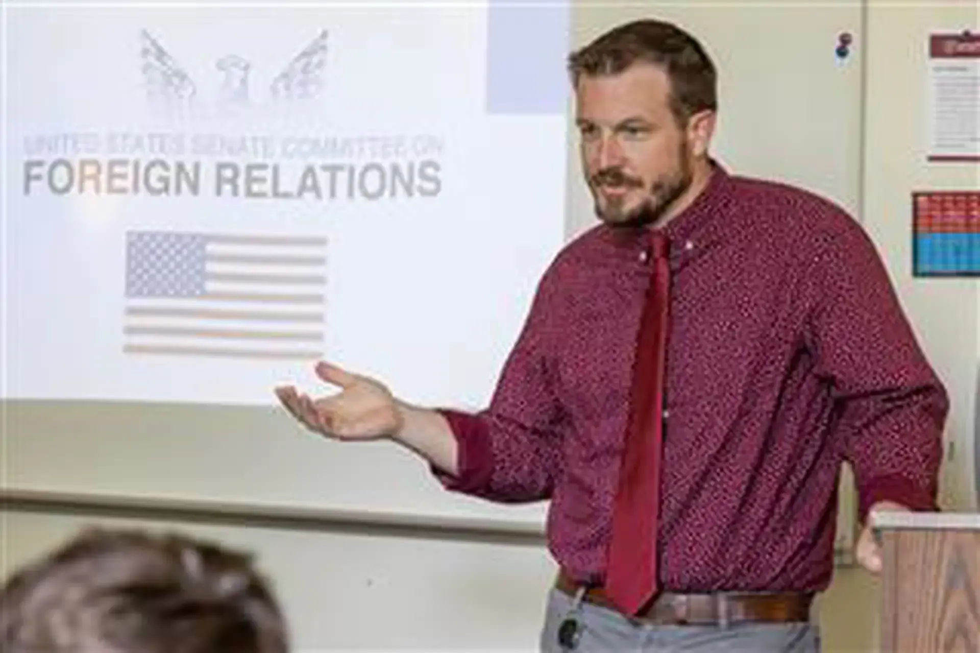 Matt McCarter leading a Social Studies class. A slide projected on a whiteboard reads 'Foreign Relations'.