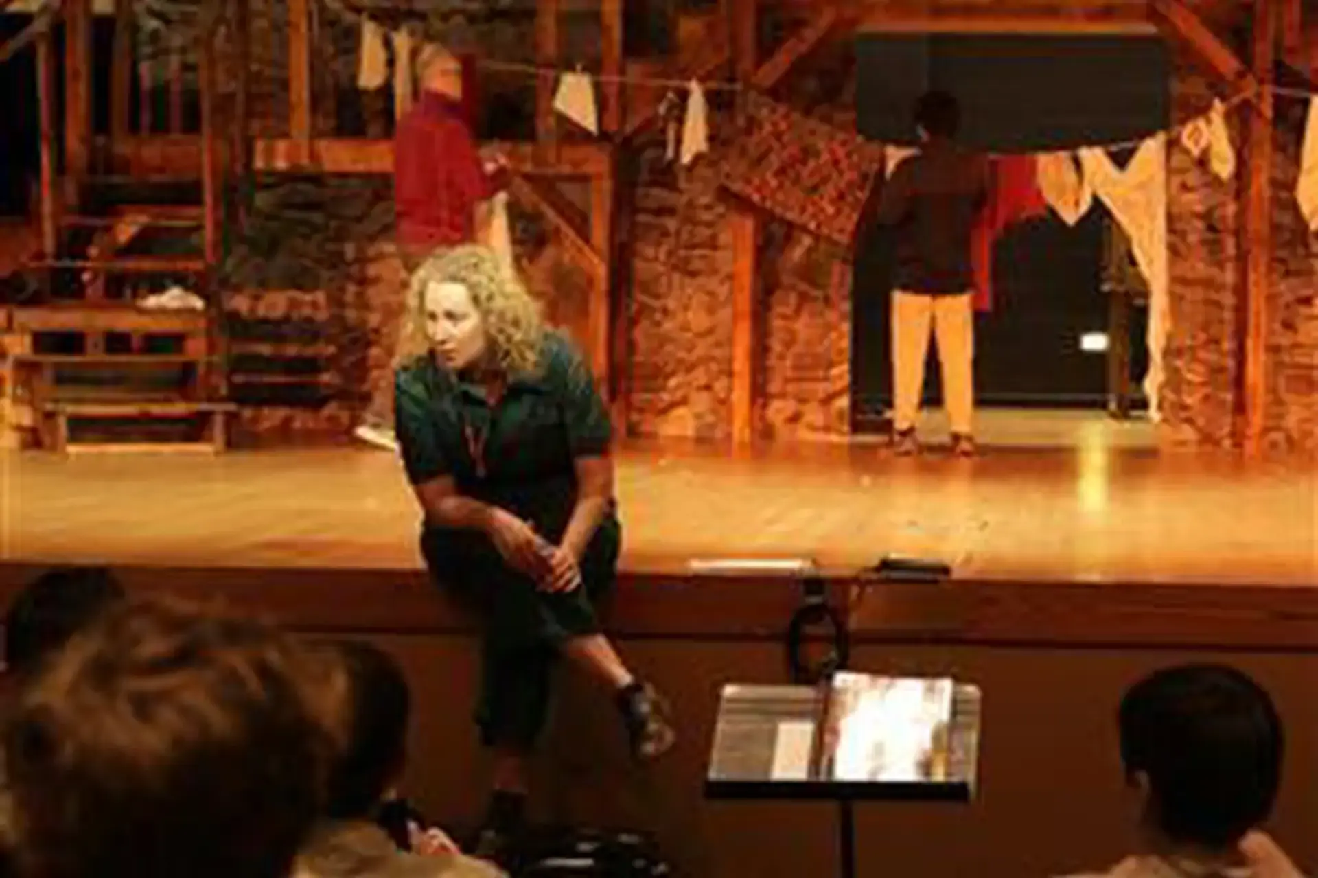 Samantha Pierce sitting on the edge of a stage holding a theatrical set, speaking to students.