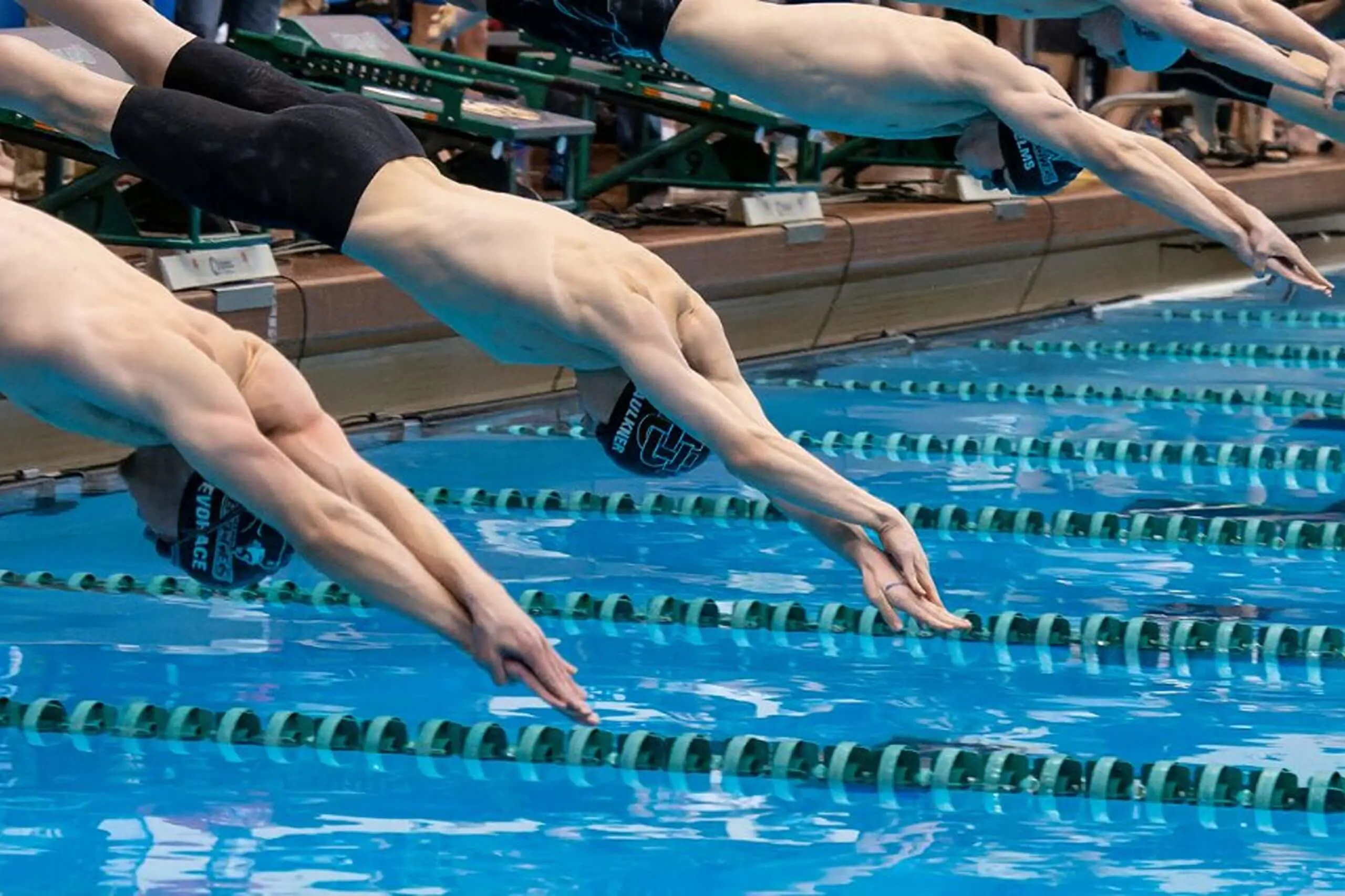 University School students wearing swimming caps and goggles dive into a pool.