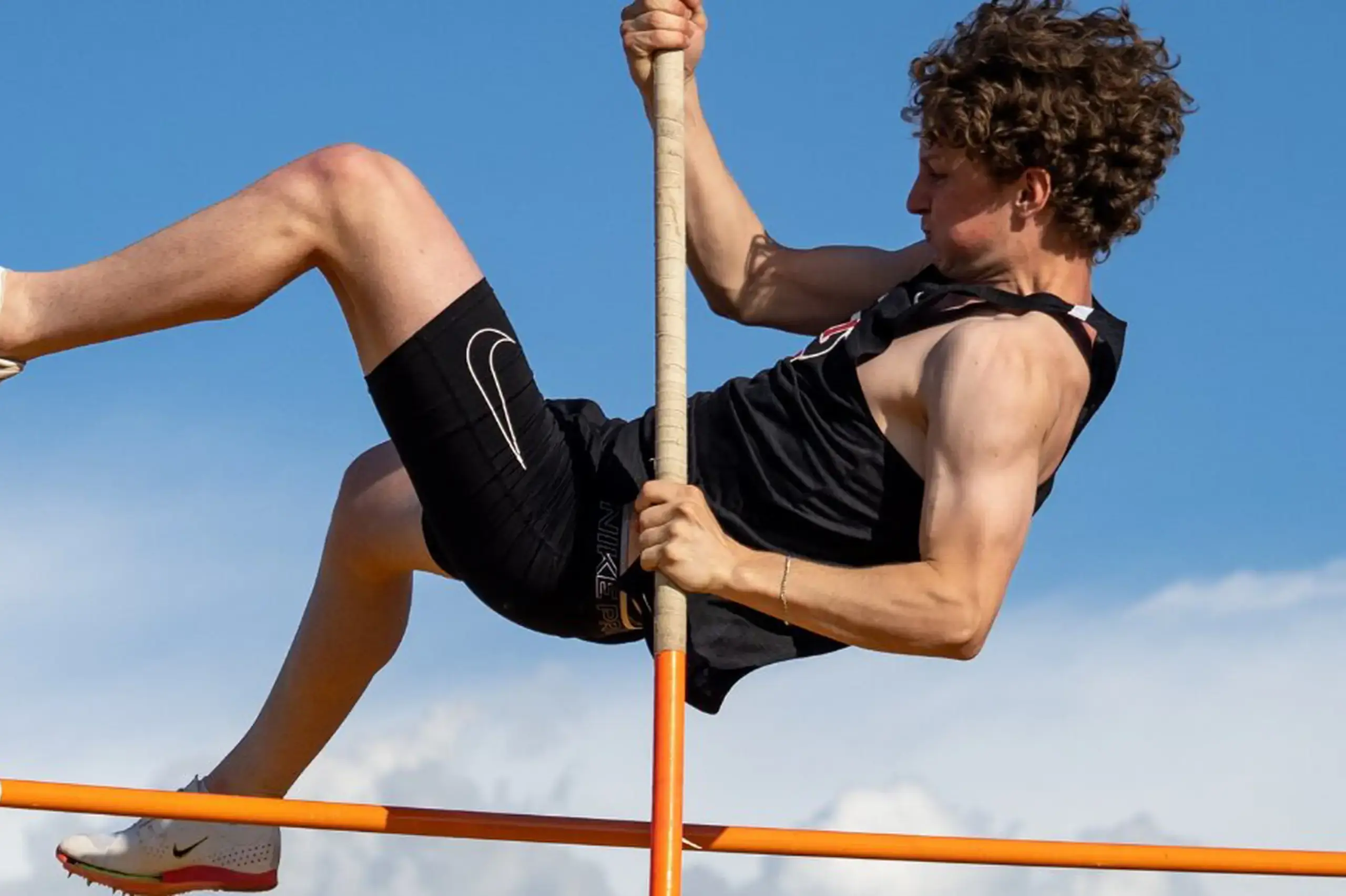 University School student taking part in a high jump, using a vaulting pole to propel themself over the bar.