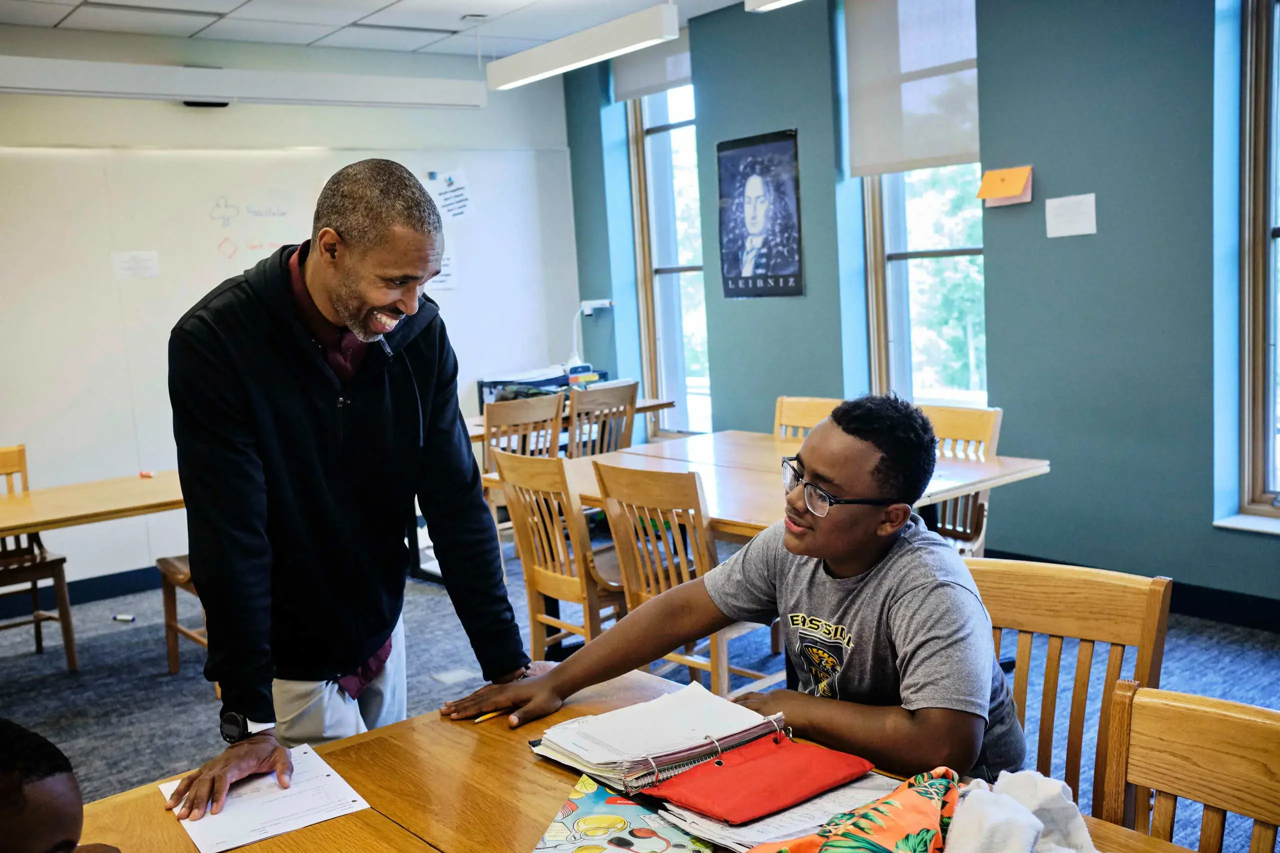University School Teacher and student discussing work in class, smiling and engaged.