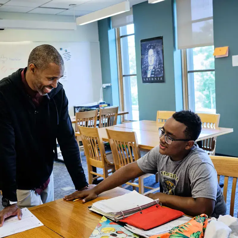 University School Teacher and student discussing work in class, smiling and engaged.