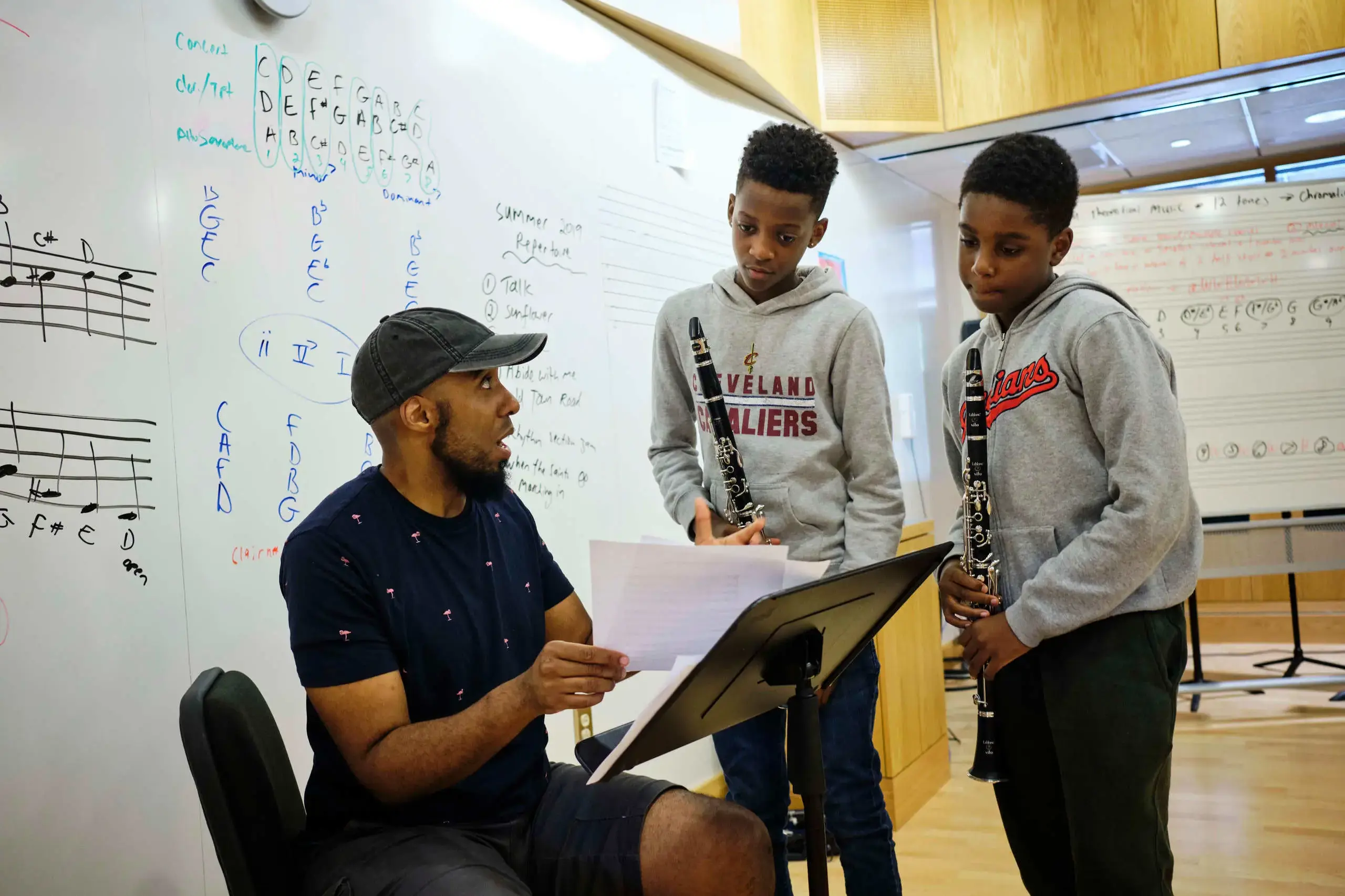 University School Students holding clarinets discussing the music score with a teacher in a music class.