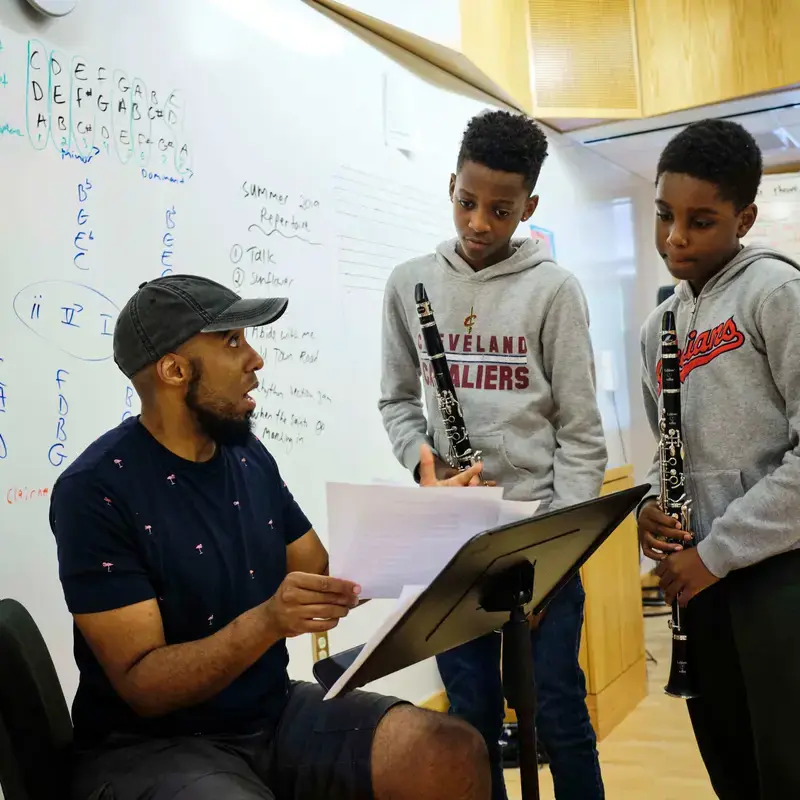 University School Students holding clarinets discussing the music score with a teacher in a music class.
