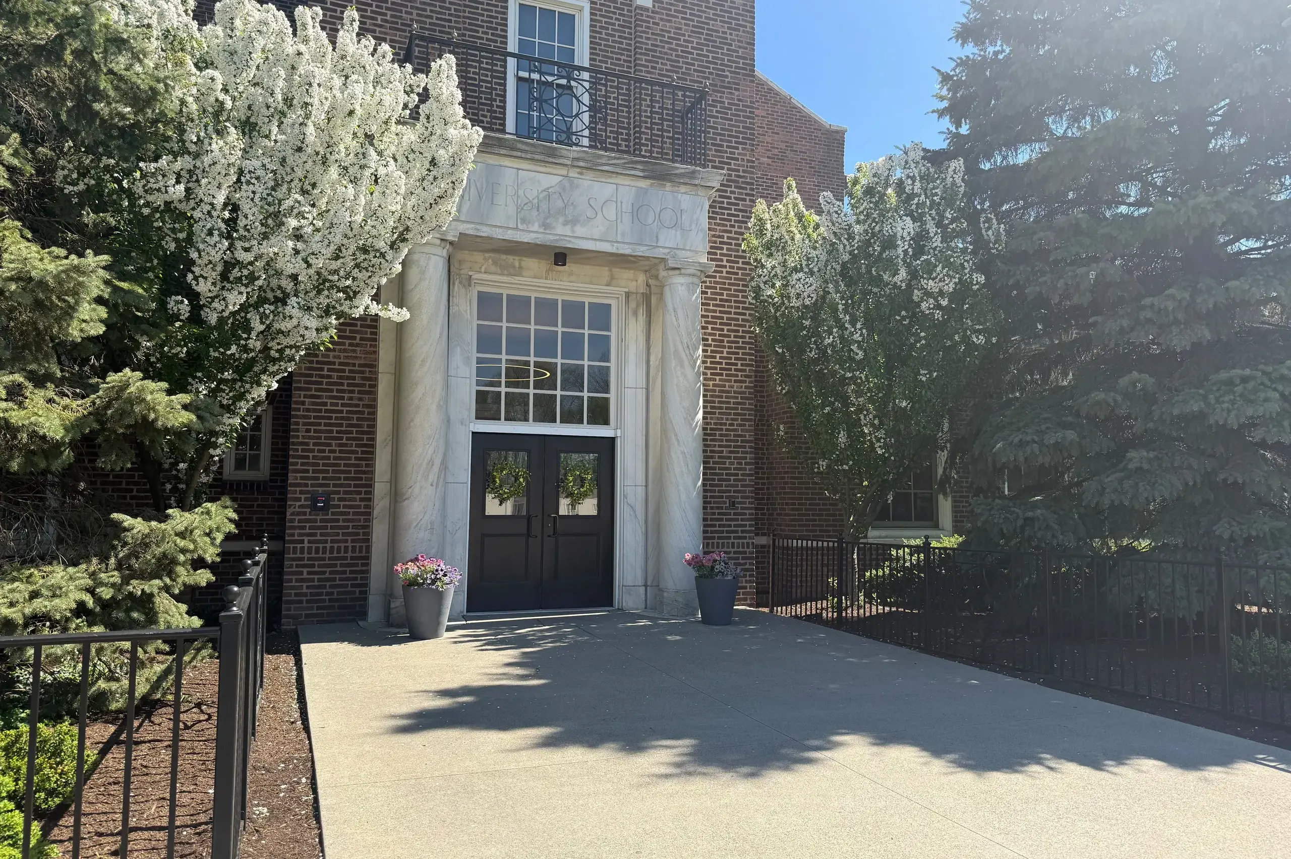 University School Shaker Campus Building Doorway in sunshine, surrounded by flowers and trees.