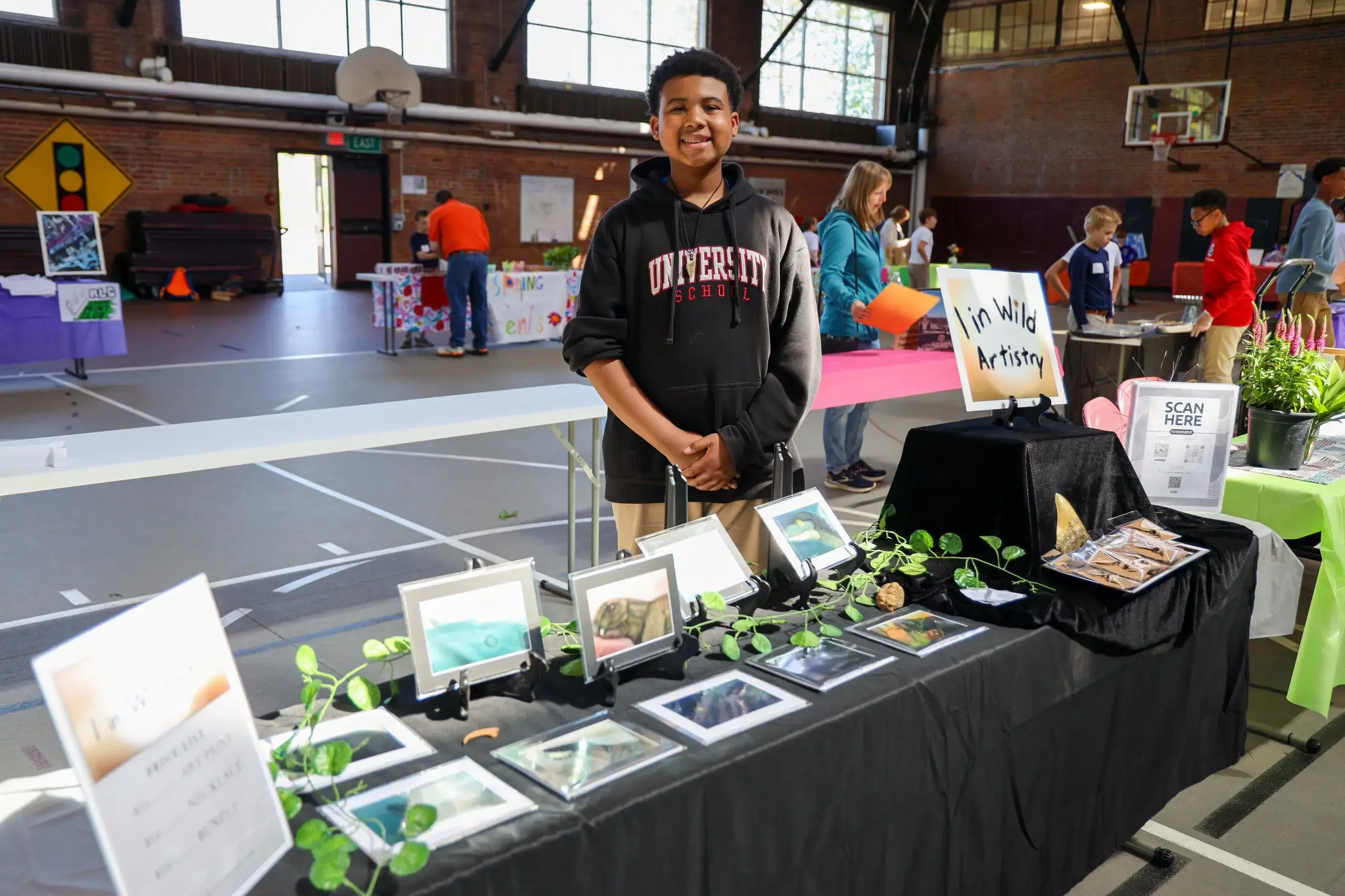 University School student standing with a display of their original artworks for sale as part of the Anderson Scholar Entrepreneurship Program.
