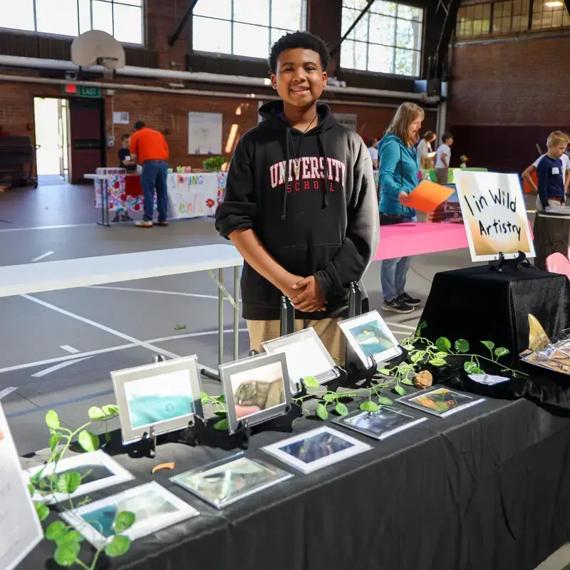 University School student standing with a display of their original artworks for sale as part of the Anderson Scholar Entrepreneurship Program.