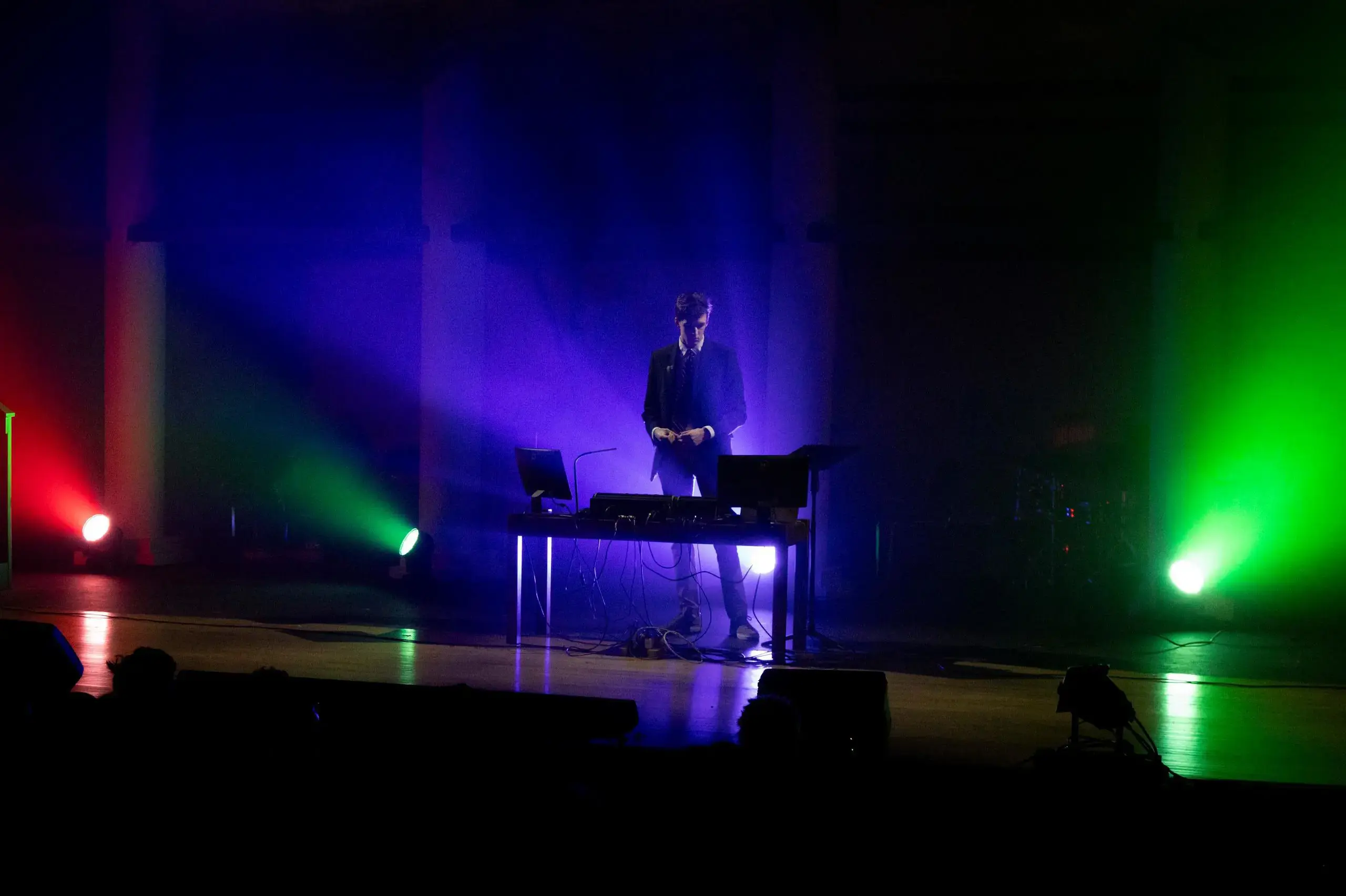 University School student giving a musical performance on stage illuminated with multicoloured beams of light.