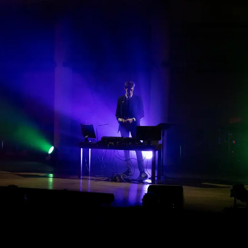 University School student giving a musical performance on stage illuminated with multicoloured beams of light.