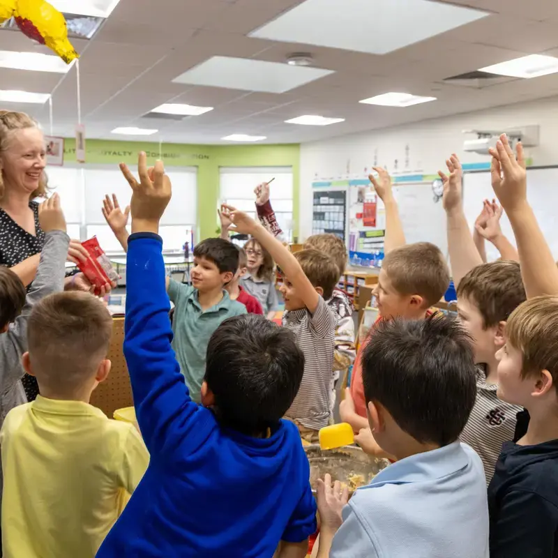 University School first graders standing around their teacher in a circle and raising their hands to answer a question.