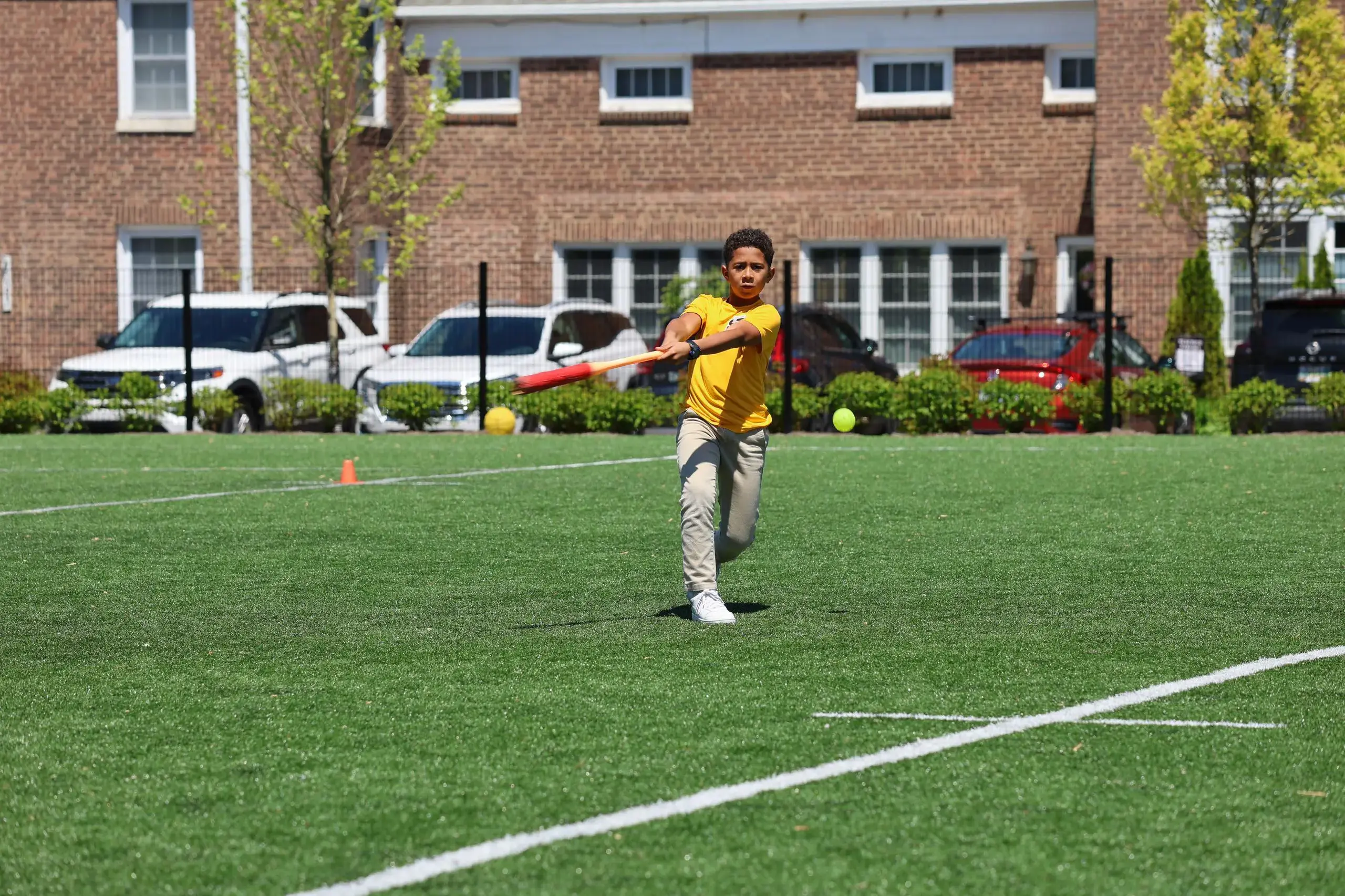 University School Middle School student hitting a ball with a baseball bat on the athletics field.