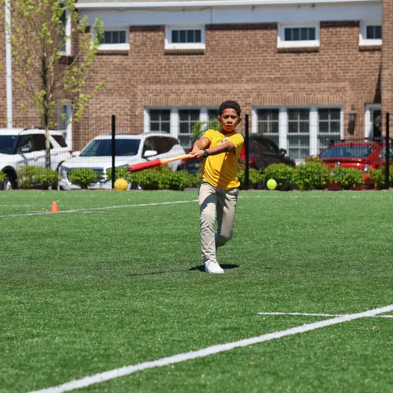 University School Middle School student hitting a ball with a baseball bat on the athletics field.